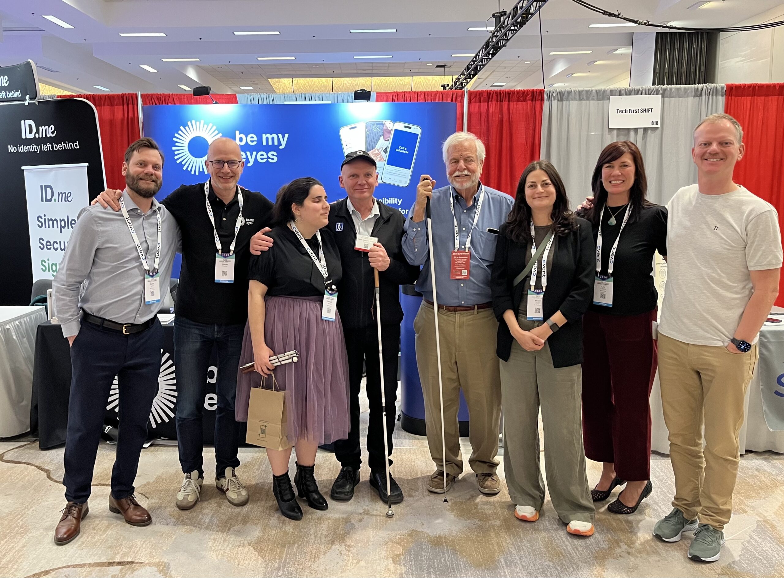 8 members of the Be My Eyes team at their booth at the CSUN Conference, 2026, smiling.