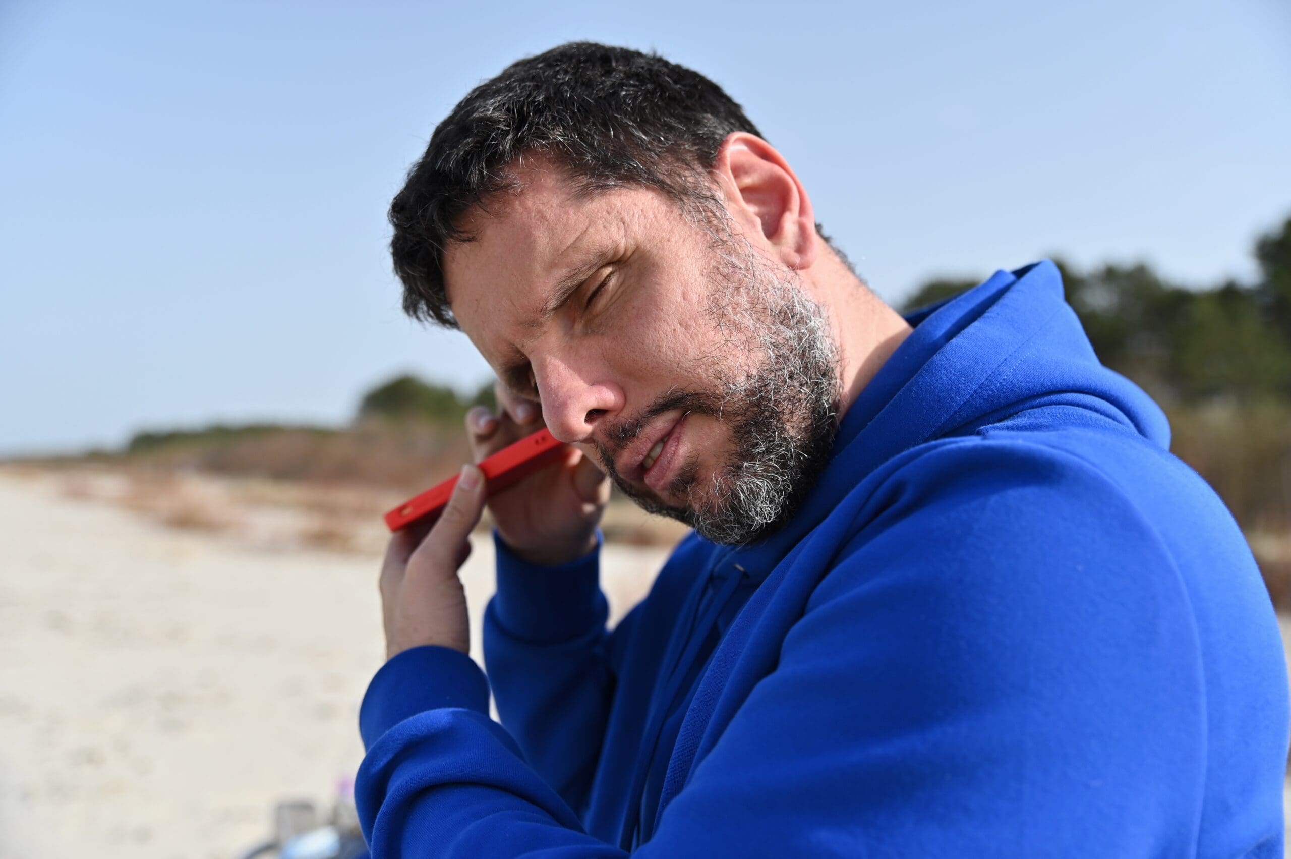 Man on a beach, holding a smartphone to his ear