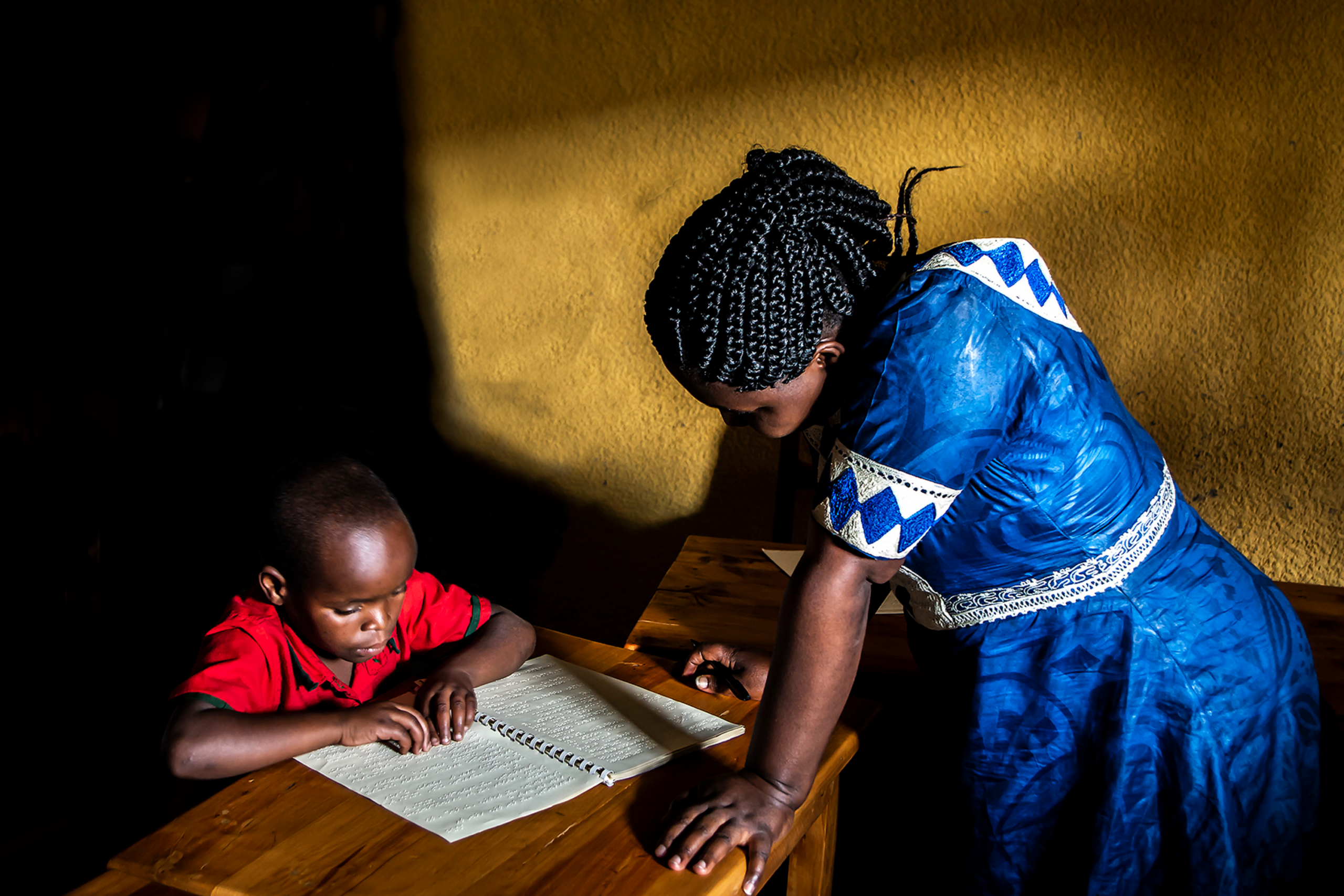 a woman stands by a young boy reading Braille