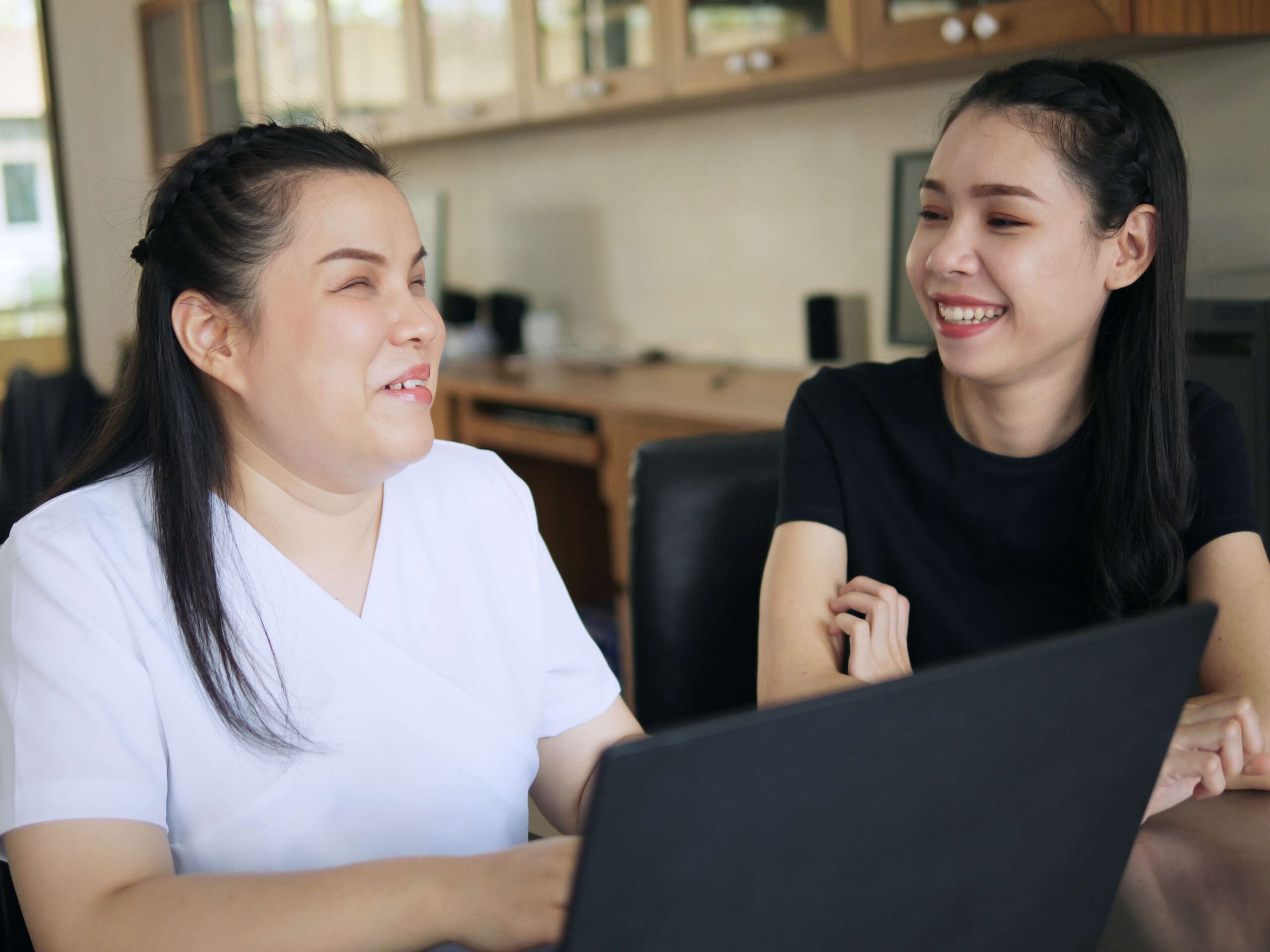 Two women sitting by a laptop, smiling.